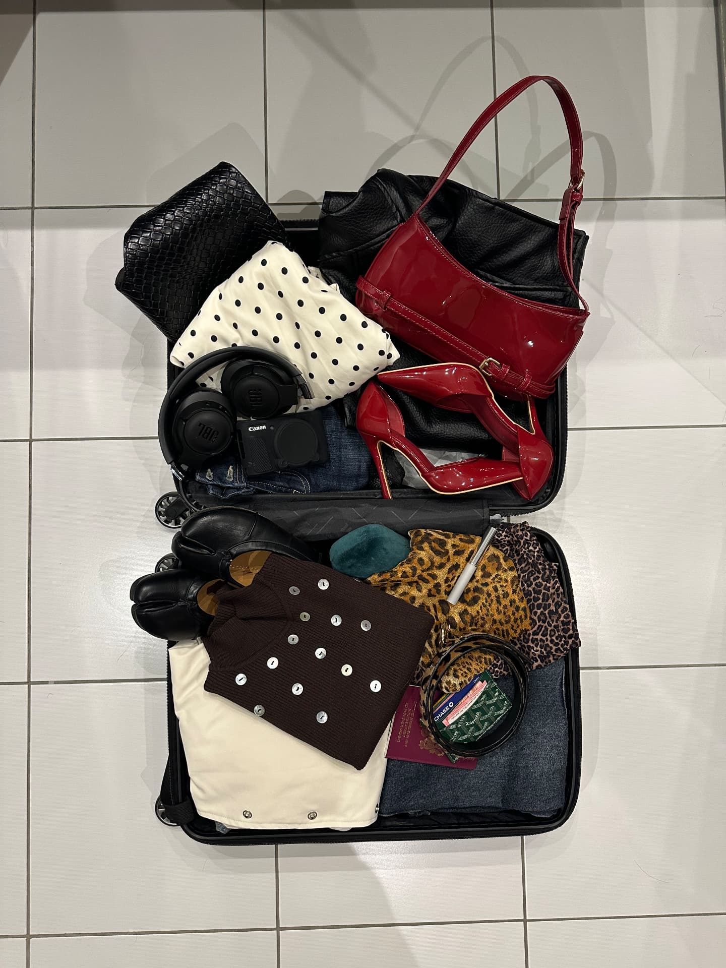 An open suitcase packed with a red patent bag and heels, leopard print, black leather and knitwear